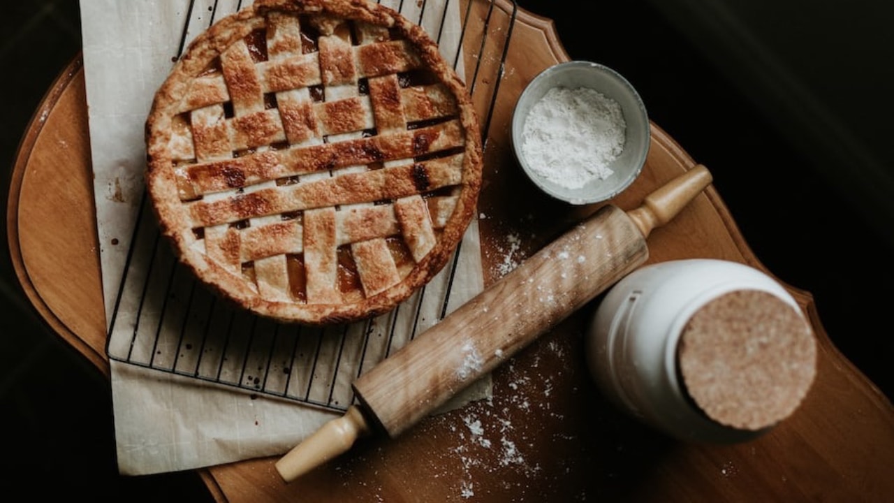 Apple pie with a rolling pin and jar of flour on a kitchen counter